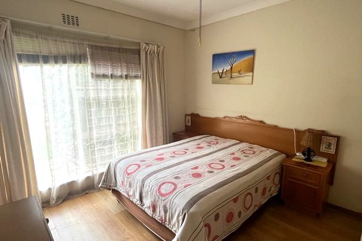 A functional bedroom featuring laminate flooring, a ceiling fan, and a sliding glass door providing natural light.
