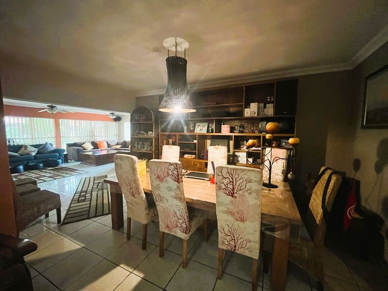 Open plan dining and living area featuring tiled flooring, a built-in wooden shelving unit, and ceiling fans.