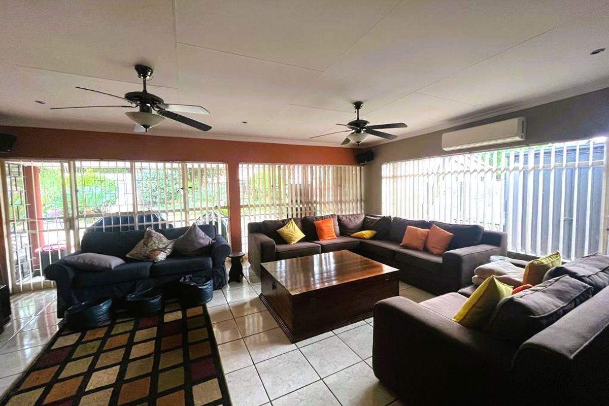 Spacious living room featuring tiled flooring, dual ceiling fans, and a wall-mounted air conditioning unit, with extensive window security bars.