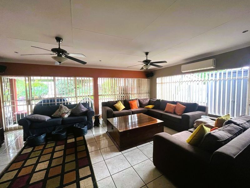Spacious living room featuring tiled flooring, dual ceiling fans, and a wall-mounted air conditioning unit, with extensive window security bars.