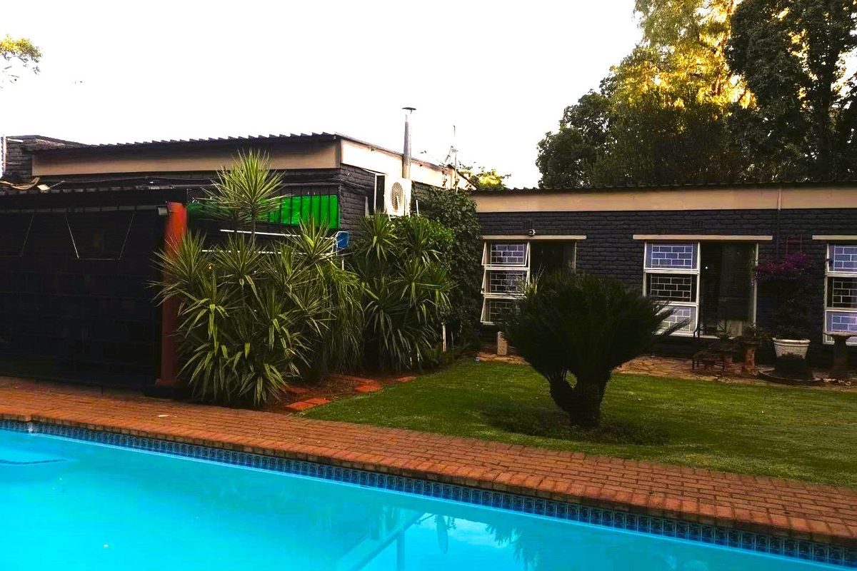 A view of the swimming pool area featuring brick coping, a well-maintained lawn, and the rear exterior facade of the house.