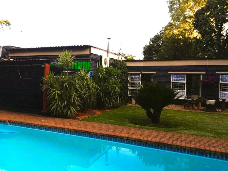 A view of the swimming pool area featuring brick coping, a well-maintained lawn, and the rear exterior facade of the house.