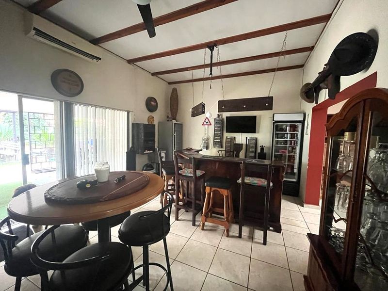 A dedicated bar area featuring a built-in counter, exposed timber ceiling beams, tiled flooring, and direct access to the outdoor space via sliding glass doors.