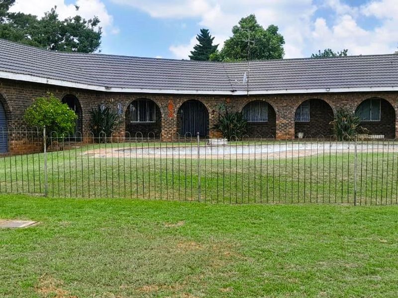 Rear view of a single-story brick house featuring a swimming pool, arched architectural details, and a large lawn area.