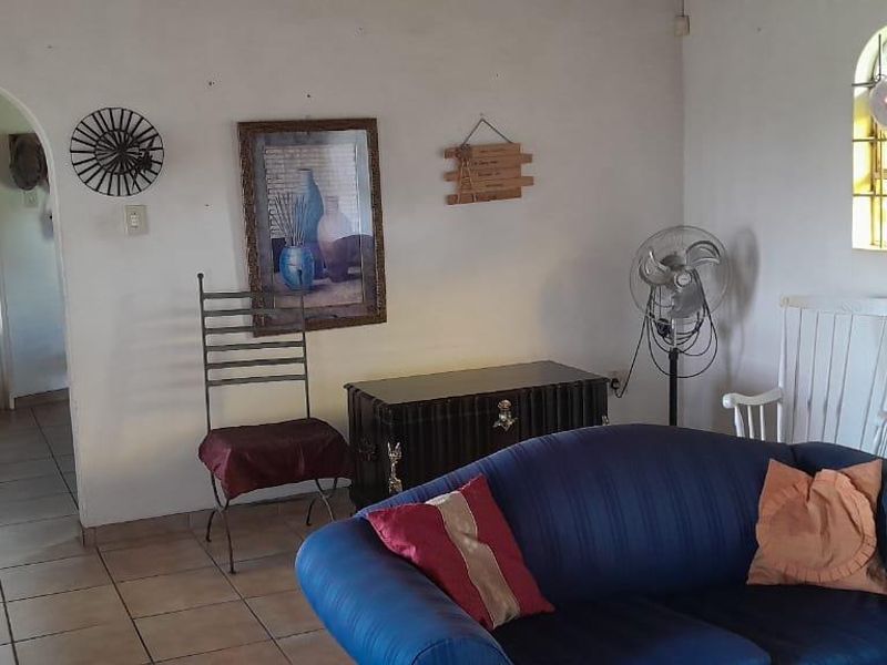 A living room featuring tiled flooring, an arched doorway leading to the kitchen, and an arched window with security bars.