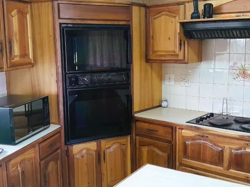 A traditional kitchen featuring wooden cabinetry, built-in oven and microwave, electric hob with extractor fan, and tiled backsplash.