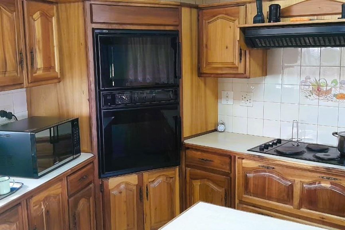 A traditional kitchen featuring wooden cabinetry, built-in oven and microwave, electric hob with extractor fan, and tiled backsplash.