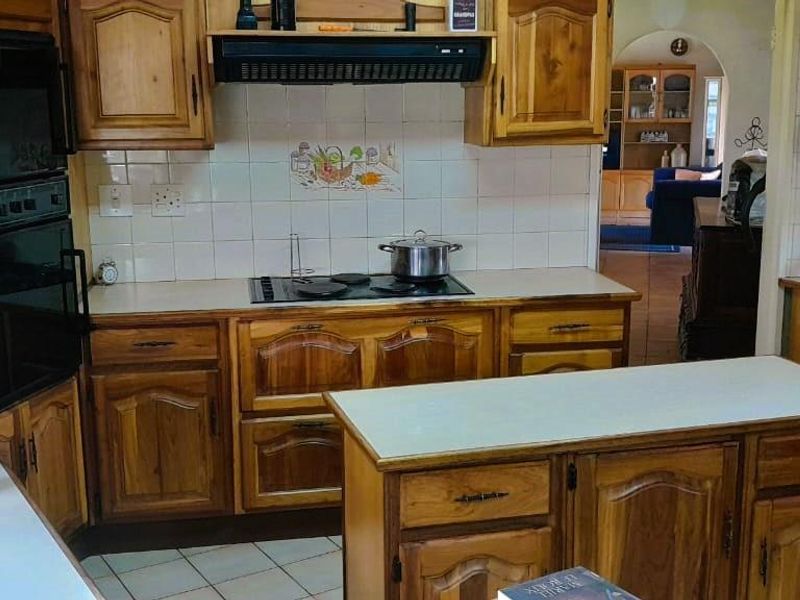 A functional kitchen featuring traditional wooden cabinetry, a built-in oven, electric hob with extractor fan, and a central kitchen island with tiled flooring.