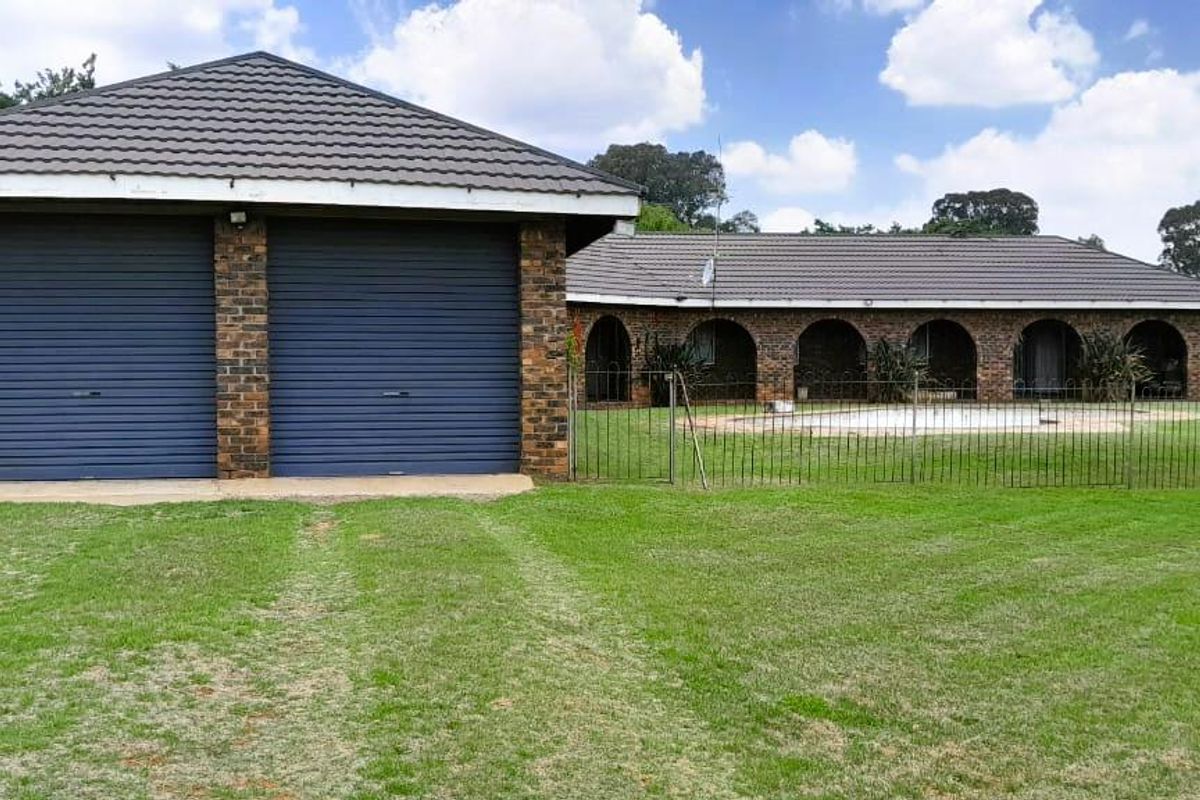 Rear view of the property featuring a double garage with roller doors, an arched patio area, and a swimming pool set within a large garden.