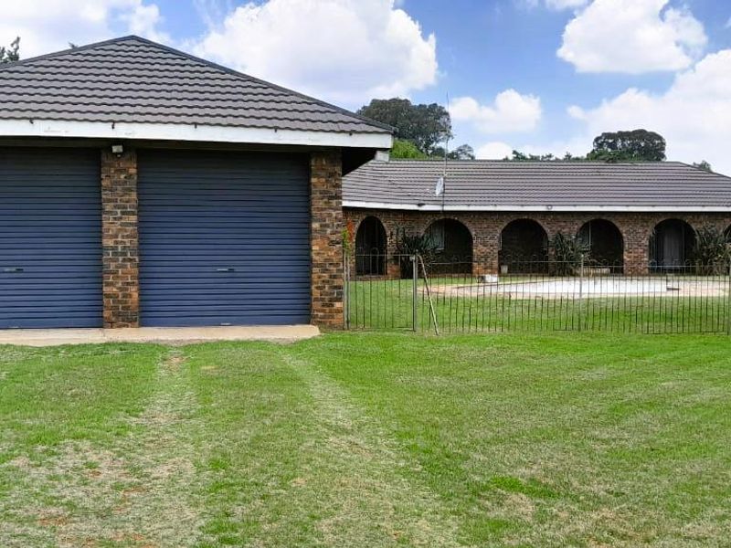 Rear view of the property featuring a double garage with roller doors, an arched patio area, and a swimming pool set within a large garden.