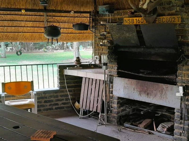 Covered outdoor patio featuring a traditional thatched roof and a large built-in brick braai area, overlooking the garden.