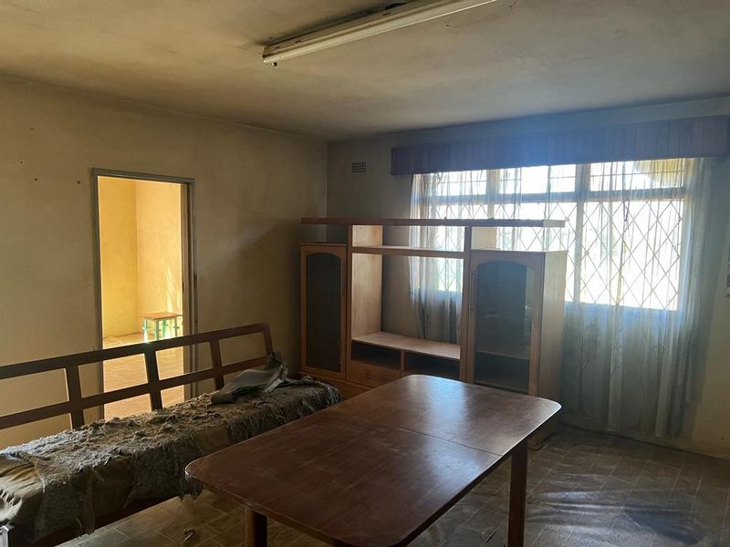 A dated living room area featuring a large window with security bars, requiring significant cosmetic updates and refurbishment of the flooring and wall finishes.