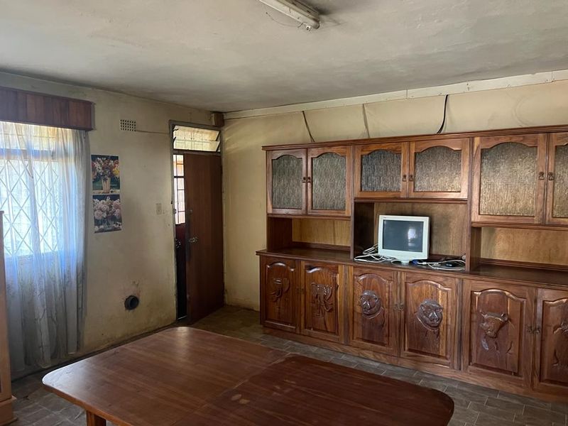 A dated living area featuring tiled floors and built-in wooden cabinetry, requiring cosmetic updates and wall repairs to improve the overall aesthetic.