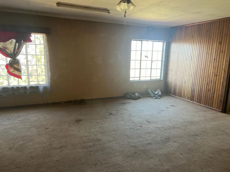 A spacious, empty living area featuring wood paneling, steel-framed windows, and original carpeting, offering a blank canvas for renovation and modernization.