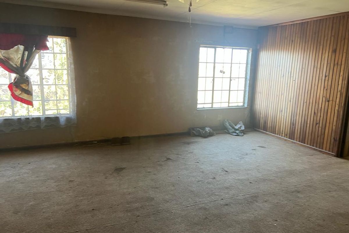 A spacious, empty living area featuring wood paneling, steel-framed windows, and original carpeting, offering a blank canvas for renovation and modernization.