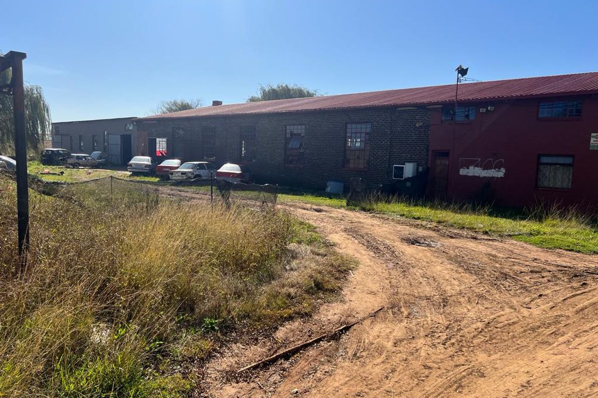 Rear view of a large industrial-style farm building featuring a corrugated metal roof and brick exterior, situated on a dirt access road.