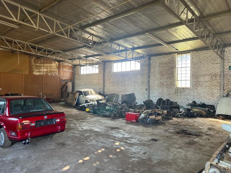 Large industrial-style garage space featuring exposed steel roof trusses, painted brick walls, and concrete flooring, suitable for workshop or storage use.