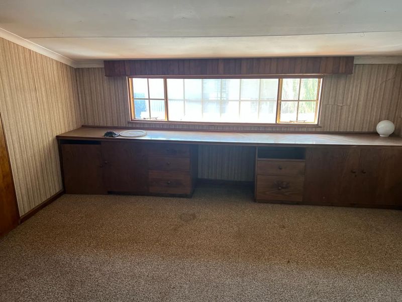A vacant office space featuring extensive built-in wooden cabinetry and a long desk area, requiring cosmetic updates to modernize the dated finishes.