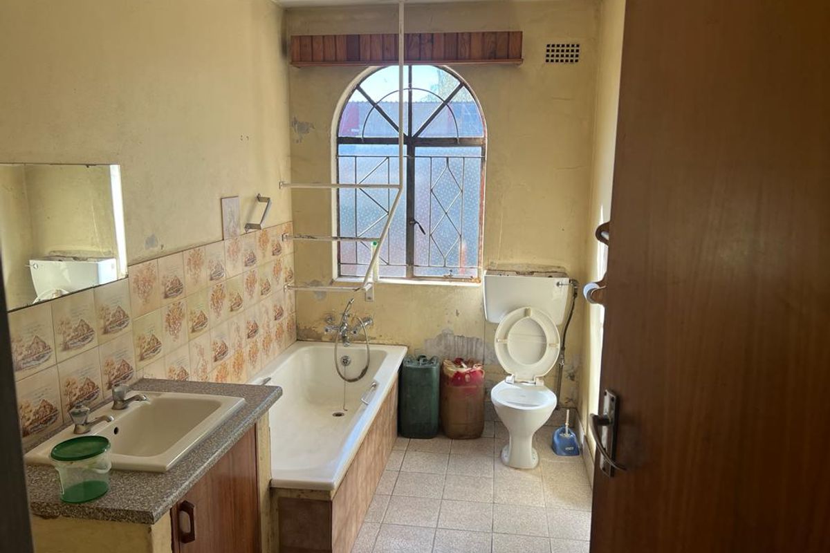 A dated bathroom featuring a built-in vanity, bathtub, and toilet, requiring significant renovation and cosmetic updates to improve its condition and functionality.