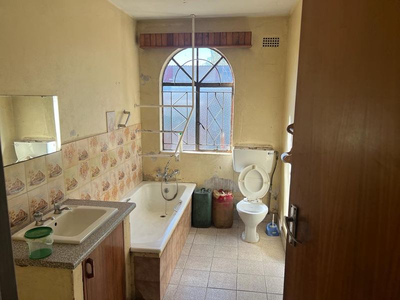 A dated bathroom featuring a built-in vanity, bathtub, and toilet, requiring significant renovation and cosmetic updates to improve its condition and functionality.