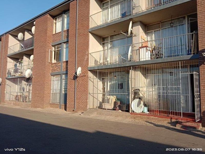 Exterior view of a multi-story apartment building featuring brick facade, balconies with metal railings, and security gates on the ground floor units.