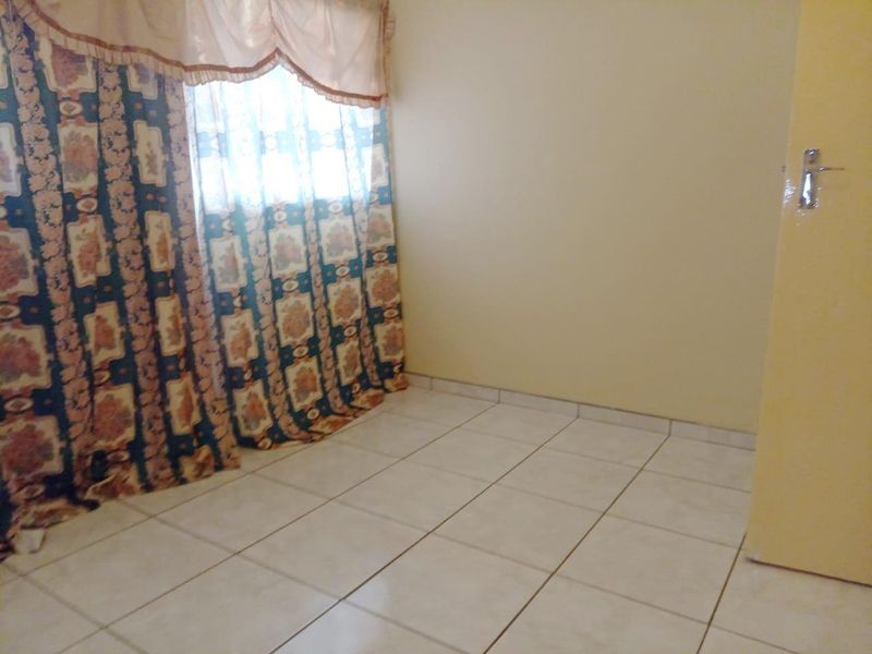 An empty bedroom featuring tiled flooring and a window with curtains.