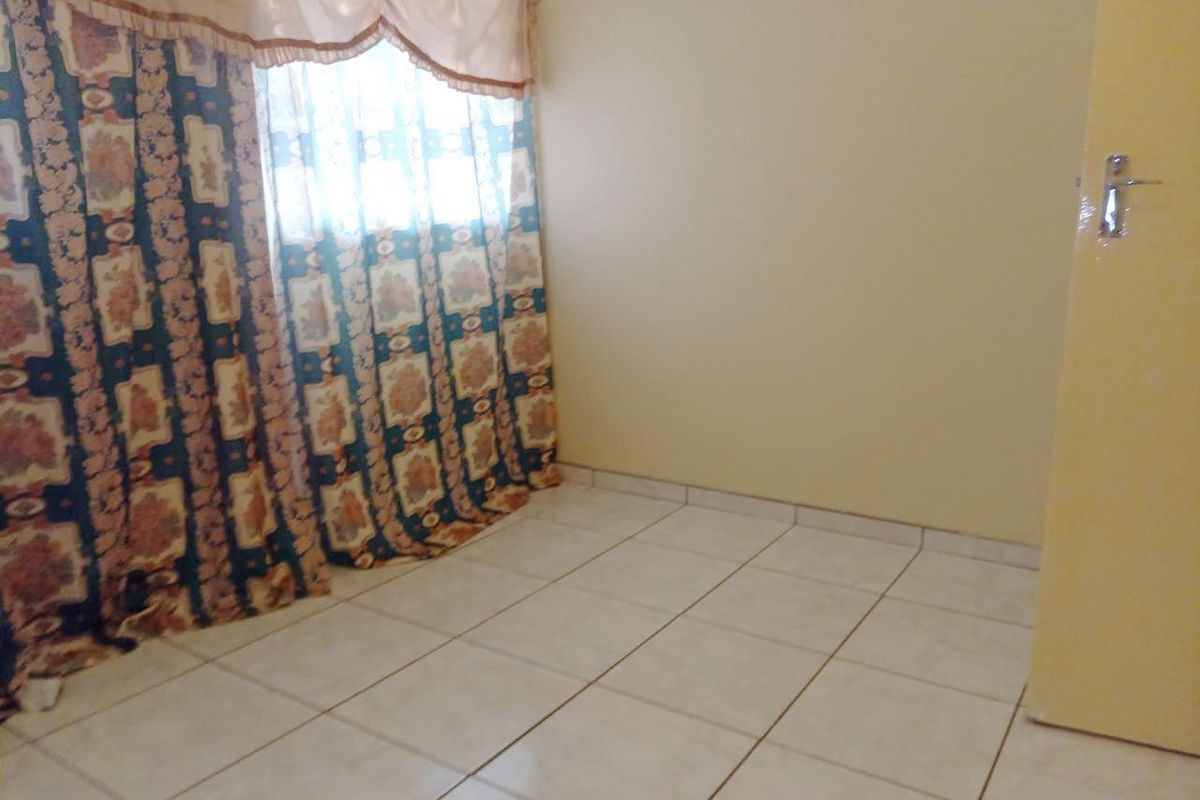 An empty bedroom featuring tiled flooring and a window with curtains.