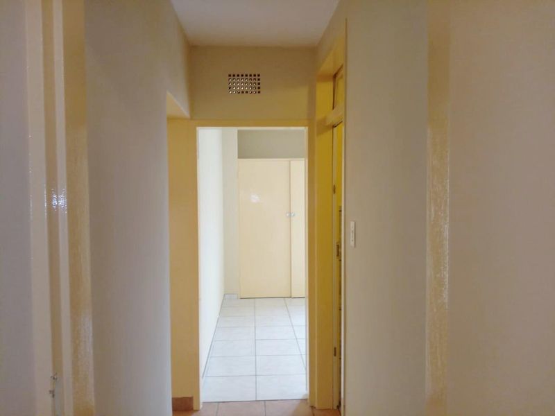 A functional hallway featuring tiled flooring, a built-in cupboard, and neutral wall finishes, providing access to adjacent rooms within the apartment.