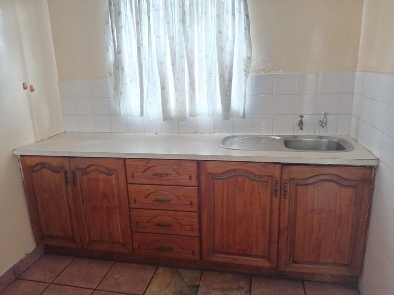 A functional kitchen area featuring traditional wooden cabinetry, a stainless steel sink, and tiled backsplash, offering a blank canvas for potential modern updates.