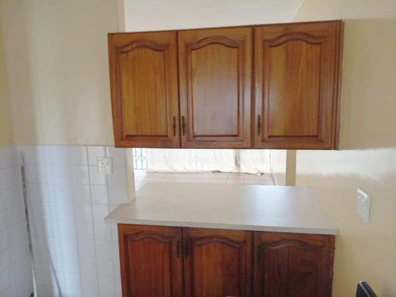 A functional kitchen area featuring traditional wooden cabinetry, a laminate countertop, and a tiled splashback, offering a clean and practical workspace.