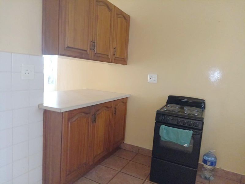A functional kitchen area featuring wooden cabinetry, laminate countertops, tiled splashbacks, and a freestanding stove.