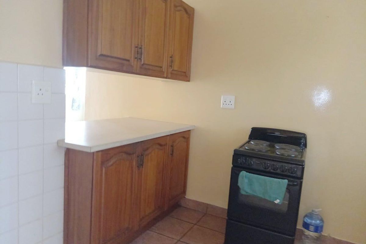 A functional kitchen area featuring wooden cabinetry, laminate countertops, tiled splashbacks, and a freestanding stove.