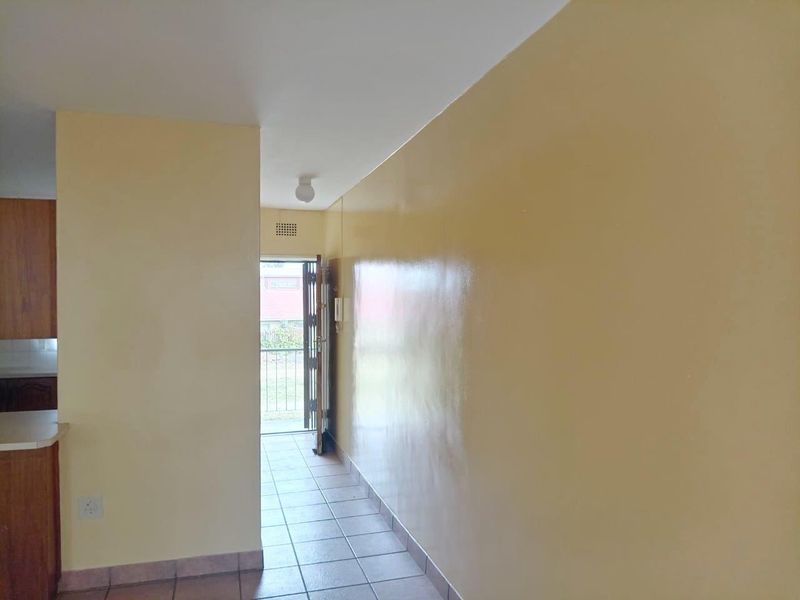 A clean, empty hallway featuring tiled flooring, an intercom system, and a security gate leading to the exterior.