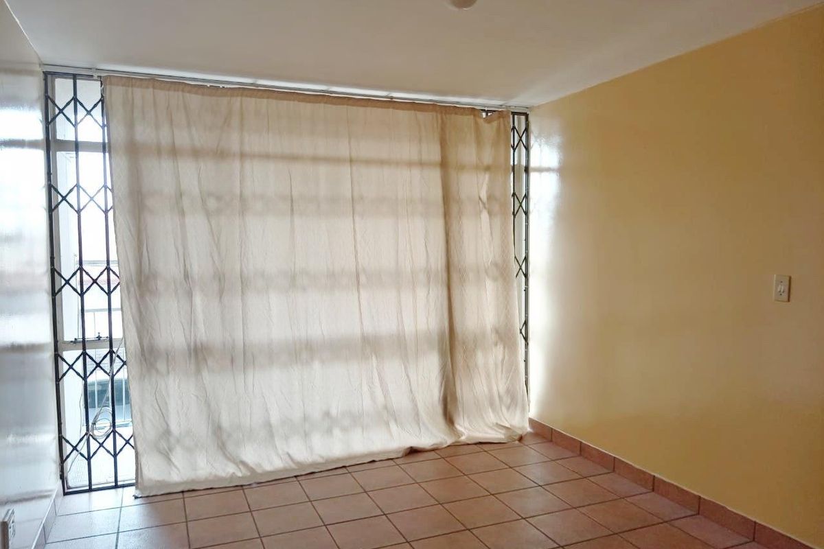 An empty living room featuring tiled flooring and a secure sliding door with an integrated security gate.