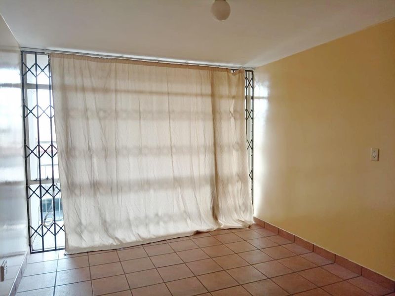 An empty living room featuring tiled flooring and a secure sliding door with an integrated security gate.