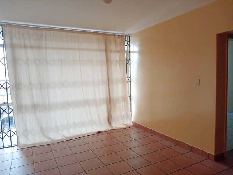 An empty living room featuring ceramic floor tiles, a sliding glass door with a security gate, and neutral wall finishes.