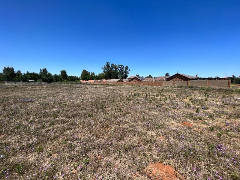 A vacant residential plot featuring natural grass coverage and a perimeter brick boundary wall, offering a clear space for future development.