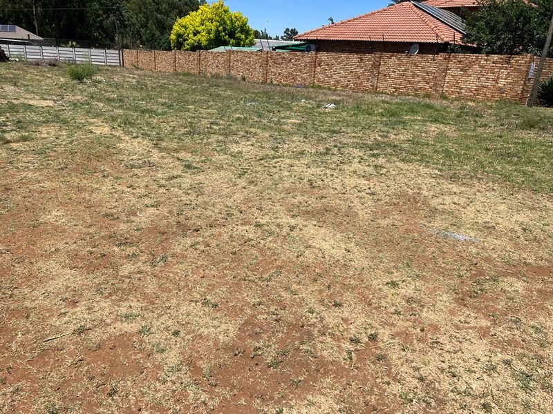 A vacant residential plot featuring dry grass and a brick perimeter wall, offering a clear space for future development.