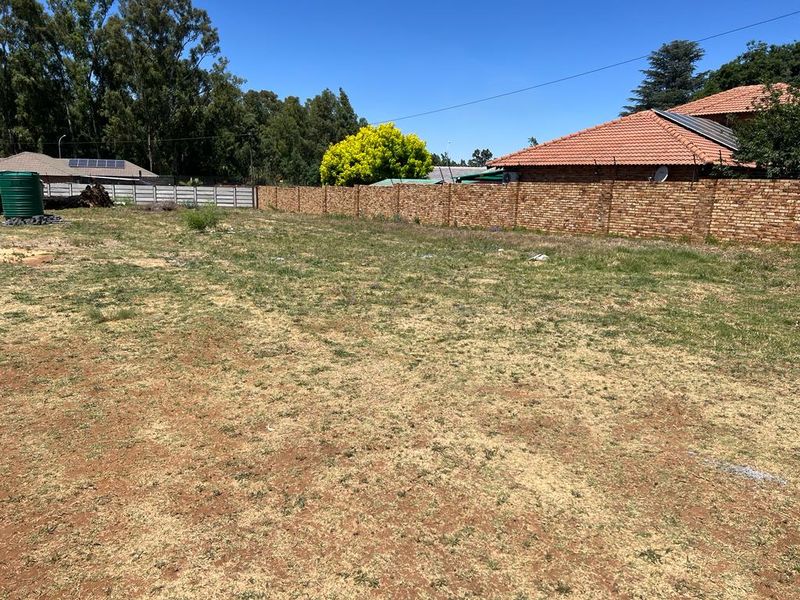 A vacant residential plot featuring a perimeter brick wall and a water storage tank, offering a clear space for future development.