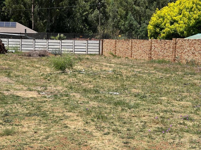 A vacant residential plot featuring a mix of precast concrete and face brick boundary walls with established trees in the background.