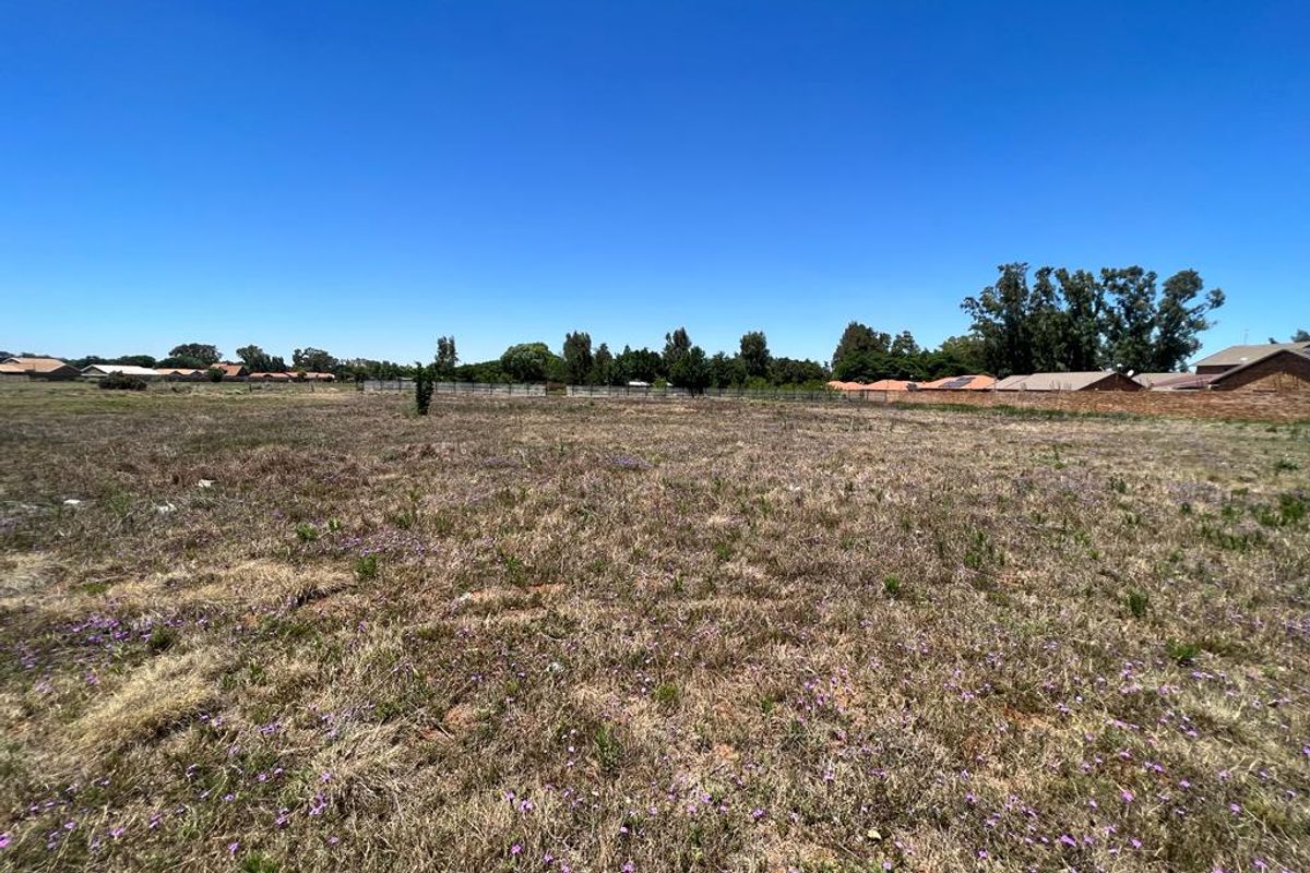 A wide-angle view of a vacant residential plot featuring natural grass cover and perimeter boundary walls in a suburban setting.