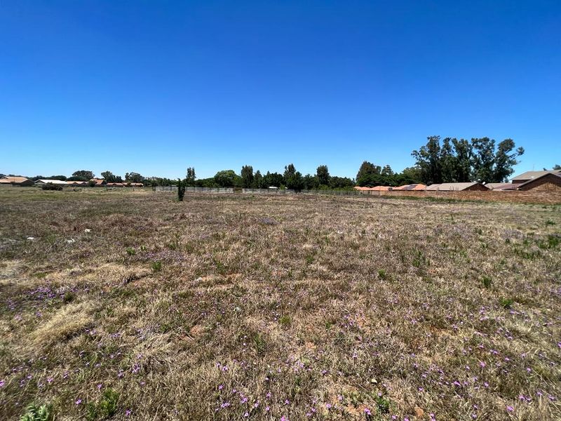 A wide-angle view of a vacant residential plot featuring natural grass cover and perimeter boundary walls in a suburban setting.