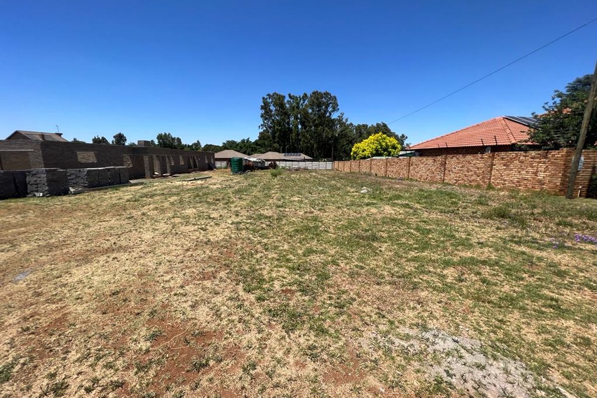 A vacant residential plot featuring a brick boundary wall, a water storage tank, and a partially constructed building structure on the property.