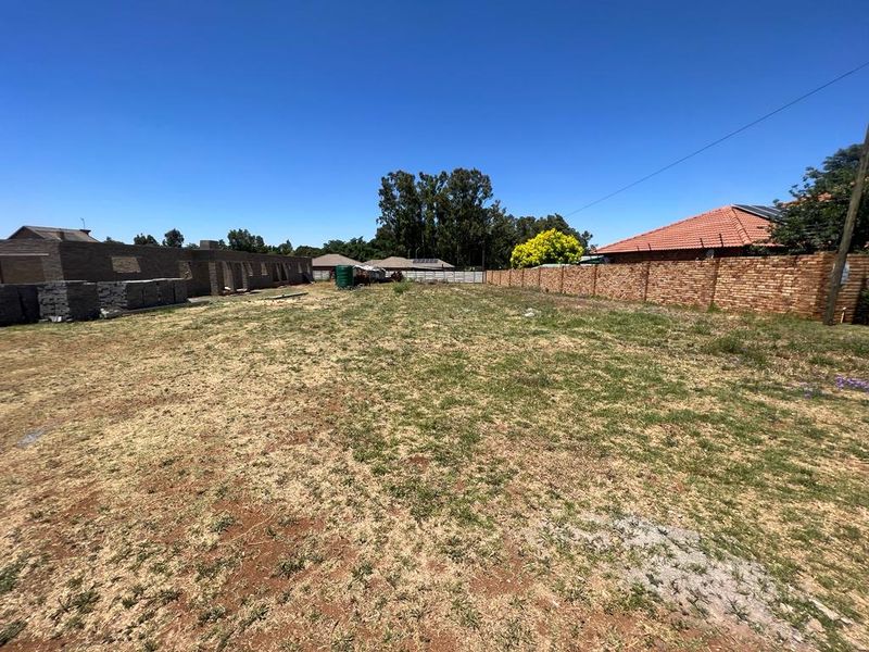 A vacant residential plot featuring a brick boundary wall, a water storage tank, and a partially constructed building structure on the property.
