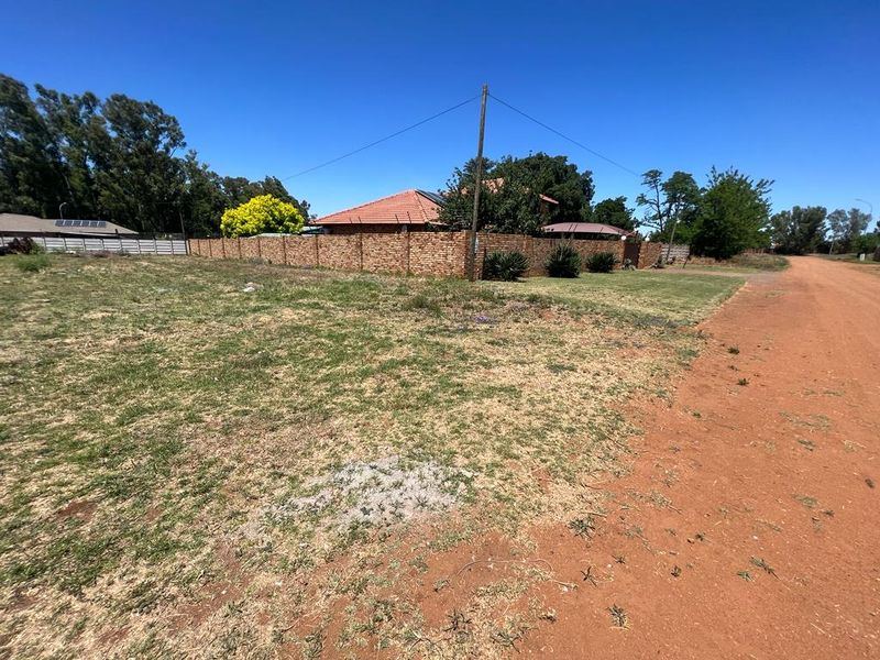 A vacant residential plot of land featuring a dirt road frontage and an existing brick boundary wall.