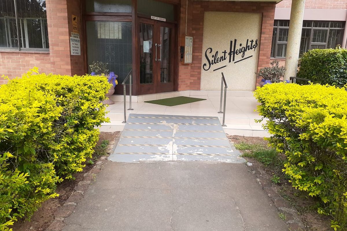 Front entrance of Silent Heights apartment building featuring a brick facade, access ramp with handrails, and intercom system.