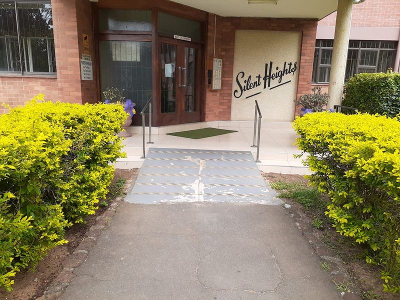 Front entrance of Silent Heights apartment building featuring a brick facade, access ramp with handrails, and intercom system.