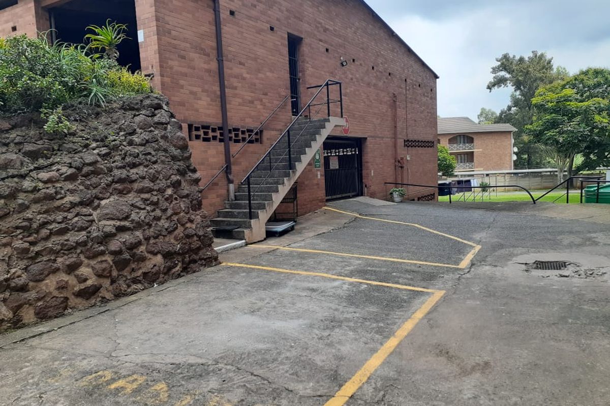 Exterior view of the apartment building featuring a brick facade, concrete staircase, and paved parking area with a security gate.
