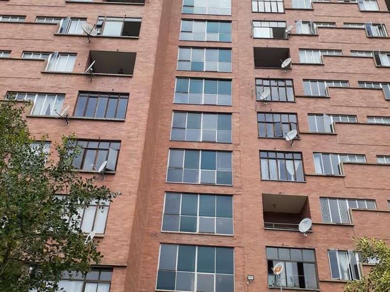 A multi-story apartment building facade featuring red brick construction, numerous windows, and multiple satellite dishes installed on the exterior.