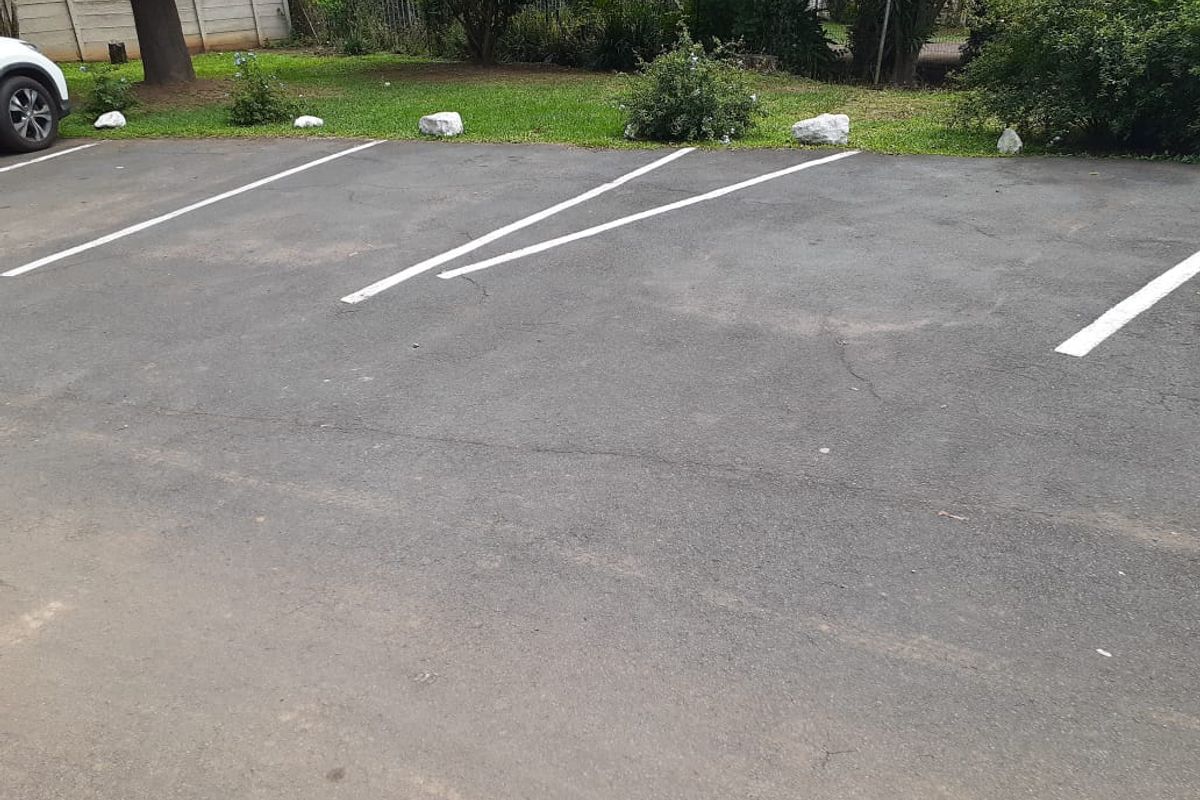 An outdoor asphalt parking area with marked bays and a boundary wall in the background.